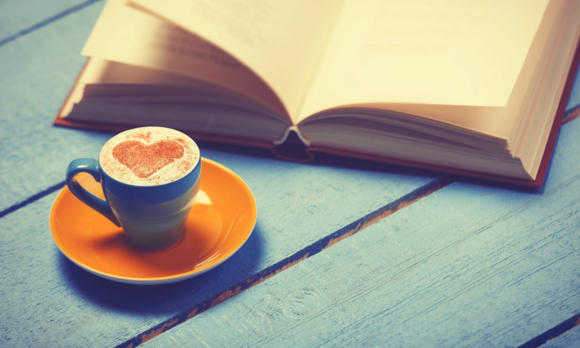 Cup of coffee with book on blue wooden table.